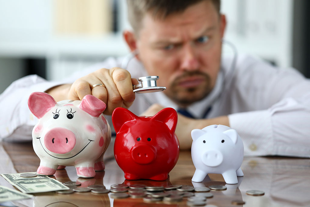 Funny businessman listen three piggybanks for cash